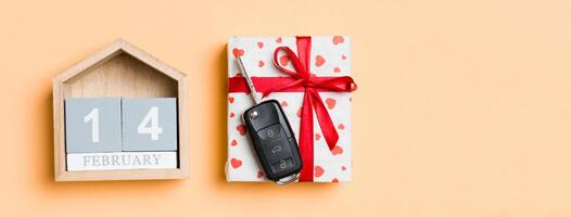 Top view of car key on a gift box with red hearts and festive calendar on colorful background. The fourteenth of february. Present for Valentine's Day concept photo