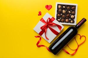 Bottle of red wine on colored background for Valentine Day with gift and chocolate. Heart shaped with gift box of chocolates top view with copy space photo