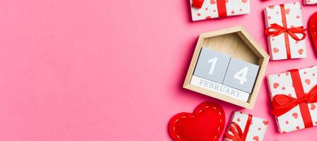Holiday composition of gift boxes, wooden calendar and red textile hearts on colorful background with empty space for your design. The fourteenth of February. Top view of Valentine's Day concept photo