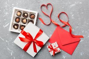 Envelope on colored background for Valentine Day with gift box and chocolate. Heart shaped with gift box of chocolates top view with copy space photo