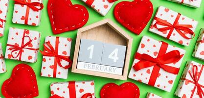 Top view of gift boxes, wooden calendar and red textile hearts on colorful background. The fourteenth of february. St Valentine's day concept with copy space photo