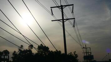Electrical poles and electrical wires on the side of the road There is a sunset sky in the background photo