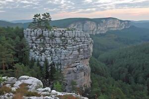 A plate rock formation overlooks pine forests, high cliffs, and white rocks adorned with green vegetation, all bathed in the soft light of dawn on a summer evening photo