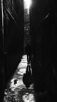 A shadowy figure looms in the distance creating a sense of unease and uncertainty in the confined space of the alleyway. Black and white art. photo