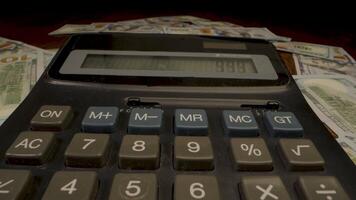 A calculator sits on a pile of US dollar bills. The calculator's display shows a number, and the buttons are visible. video