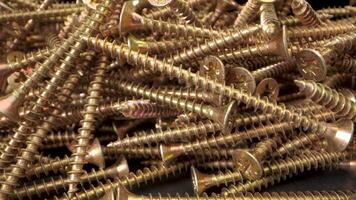 cerca arriba ver de un pila de oro tornillos. el empulgueras son arreglado en un aleatorio modelo y son iluminado por un brillante ligero. el capturas detalles de el tornillos, incluso el hilos y el cabezas video