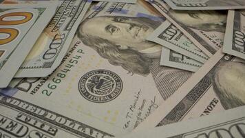 A close up shot of a stack of hundred dollar bills. The dollar bills are in various states of disarray. The bills in focus, with the faces of Benjamin Franklin visible on several of the bills. video