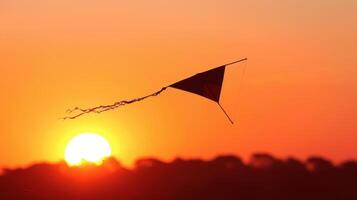 The sun setting behind a silhouette of trees a single kite with a long streaming tail flying against the orange and pink sky photo