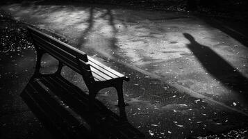 A persons shadow looming over an empty park bench a subtle reminder of the absence of human connection. Black and white art. photo