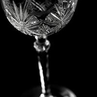 A closeup shot of a crystal wine glass the intricate patterns in its stem reflecting in the cleart.liquid inside. Black and white art. photo