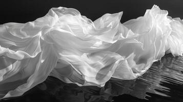 The rippling waves of a lake contrast with the stillness of the windblown fabric floating atop it. Black and white art. photo