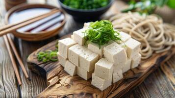 A wooden ting board with neatly stacked slices of tofu ready to be added to a dish of soba noodles photo