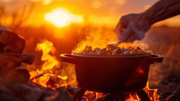 A person using a Dutch oven to cook a hearty stew while the sun sets behind them in a vibrant orange sky photo