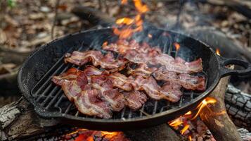 The sound of sizzling bacon fills the campsite as it slowly crisps over an open fire photo