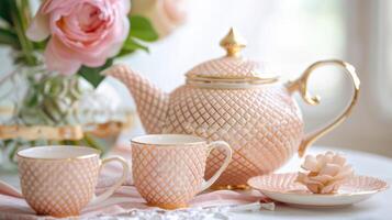 A dainty teapot in a soft peach color featuring a delicate lattice pattern and a goldaccented lid displayed alongside two tea cups in a matching hue with a subtle floral motif photo