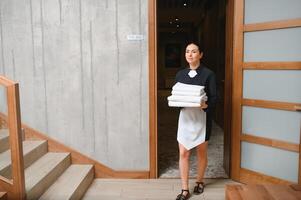 The maid is standing in the corridor of the hotel and holding clean towels photo