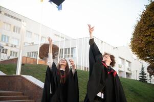 Graduates in mantles with diplomas in hands are standing near university. photo