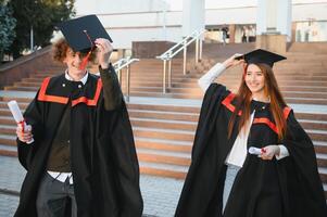 Graduates in mantles with diplomas in hands are standing near university. photo