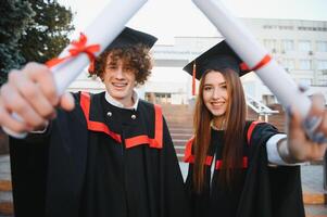 graduados en mantos con diplomas en manos son en pie cerca universidad. foto