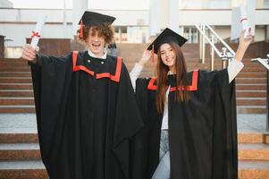 Graduates in mantles with diplomas in hands are standing near university. photo