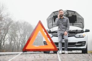 Man use a cellphone call garage in front of the open hood of a broken car on the road in the forest. Car breakdown concept. photo