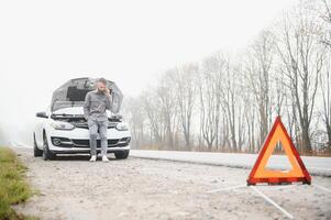 Man use a cellphone call garage in front of the open hood of a broken car on the road in the forest. Car breakdown concept. photo