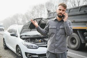 Man use a cellphone call garage in front of the open hood of a broken car on the road in the forest. Car breakdown concept. photo