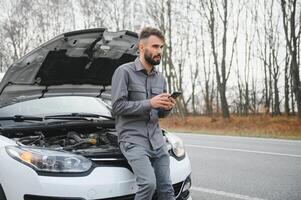 Man use a cellphone call garage in front of the open hood of a broken car on the road in the forest. Car breakdown concept. photo