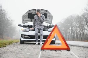 Man use a cellphone call garage in front of the open hood of a broken car on the road in the forest. Car breakdown concept. photo