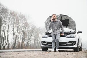Man use a cellphone call garage in front of the open hood of a broken car on the road in the forest. Car breakdown concept. photo