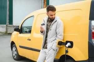 Casual man near electric car waiting for the finish of the battery charging process photo