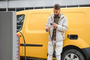 Man Holding Power Charging Cable For Electric Car In Outdoor Car Park. And he s going to connect the car to the charging station in the parking lot near the shopping center photo