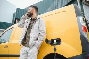 Casual man near electric car waiting for the finish of the battery charging process photo
