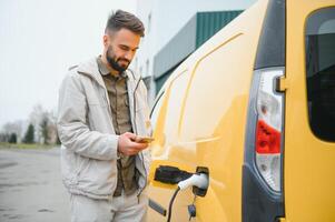 Casual man near electric car waiting for the finish of the battery charging process photo