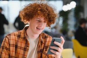 Portrait of Caucasian male freelancer in trendy apparel sitting at cafeteria table and doing remote work for programming design of public website, skilled software developer posing in coworking space. photo