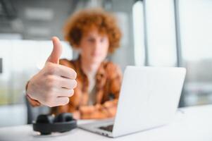 Portrait of Caucasian male freelancer in trendy apparel sitting at cafeteria table and doing remote work for programming design of public website, skilled software developer posing in coworking space. photo
