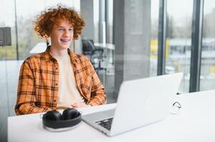 Portrait of Caucasian male freelancer in trendy apparel sitting at cafeteria table and doing remote work for programming design of public website, skilled software developer posing in coworking space. photo