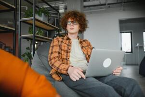 Portrait of Caucasian male freelancer in trendy apparel sitting at cafeteria table and doing remote work for programming design of public website, skilled software developer posing in coworking space. photo