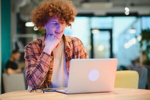 Cheerful male freelancer browsing funny content while networking in social media using netbook technology in street cafe, happy hipster guy enjoying free time for online blogging via laptop photo