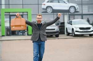 Happy buyer near the car in front of the modern avtosalon building photo