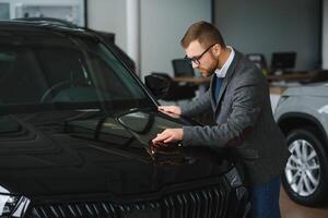 Making his choice. Horizontal portrait of a young man in a suit looking at the car and thinking if he should buy it photo