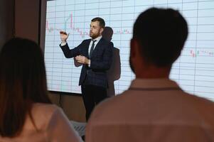 Man is standing near projector and showing graphs and business graphs. photo