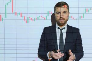 Man is standing near projector and showing graphs and business graphs. photo