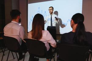 Man is standing near projector and showing graphs and business graphs. photo