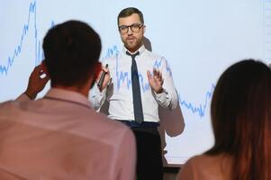 Man is standing near projector and showing graphs and business graphs. photo