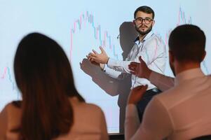 Man is standing near projector and showing graphs and business graphs. photo