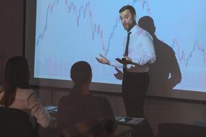 Young Businessman Explaining Graphs To His Colleagues On Projector photo