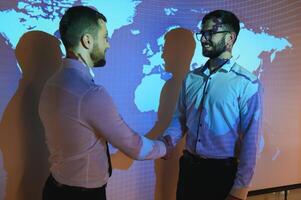 Handshake with map of the world in background. two businessmen on the background of the world map shake hands, the concept of international relations photo