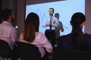Man is standing near projector and showing graphs and business graphs. photo
