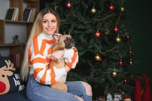 beautiful woman sits on a vintage couch with dog. on a background of a Christmas tree in a decorated room. happy new year photo